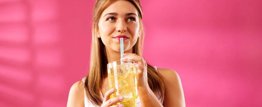 enjoyable flavored water drinks, Young woman drinking a yellow drink through a straw, holding a large glass, vibrant pink background
